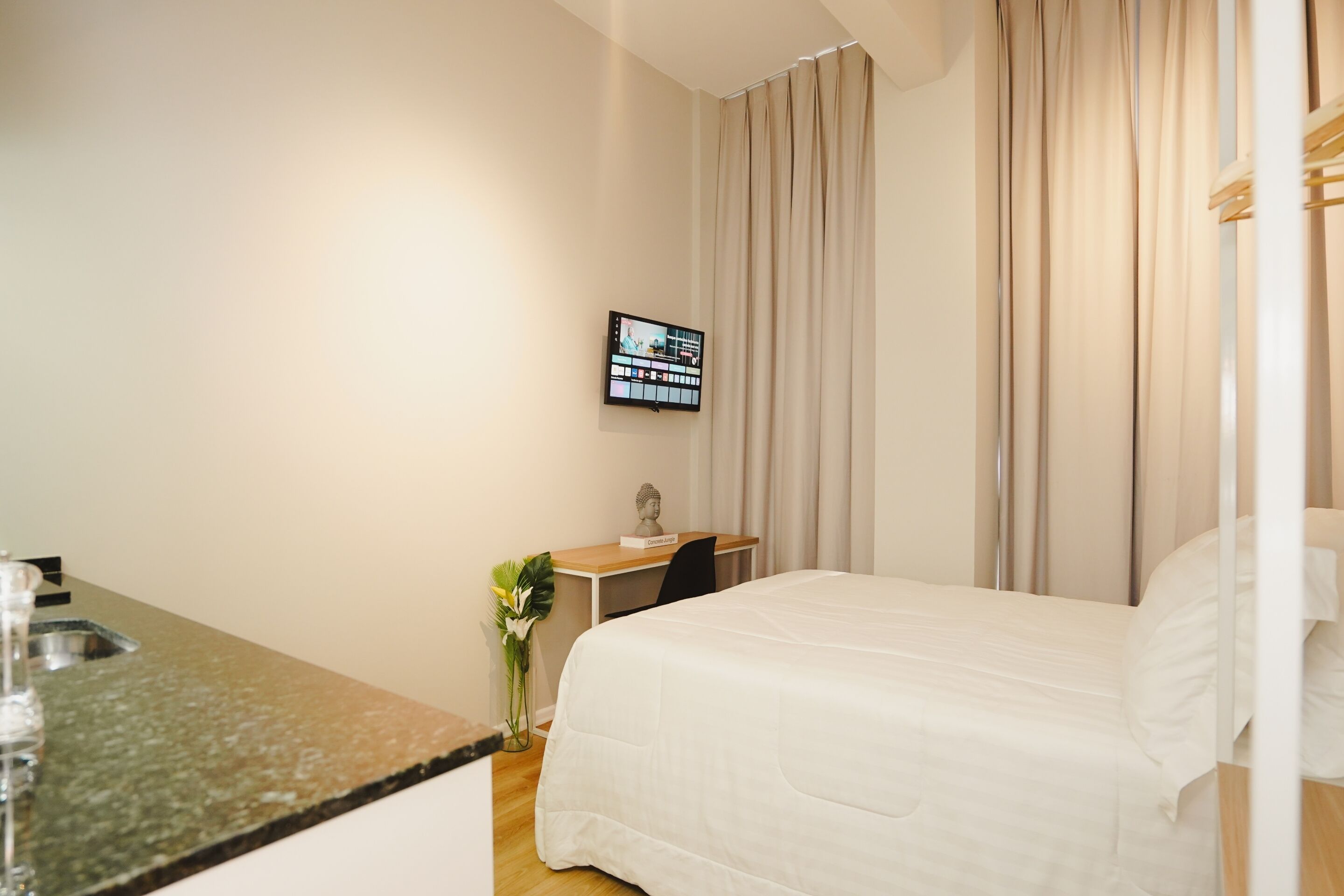 A hotel room with a bed, a desk, a television, and a window with curtains.