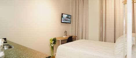 A hotel room with a bed, a desk, a television, and a window with curtains.