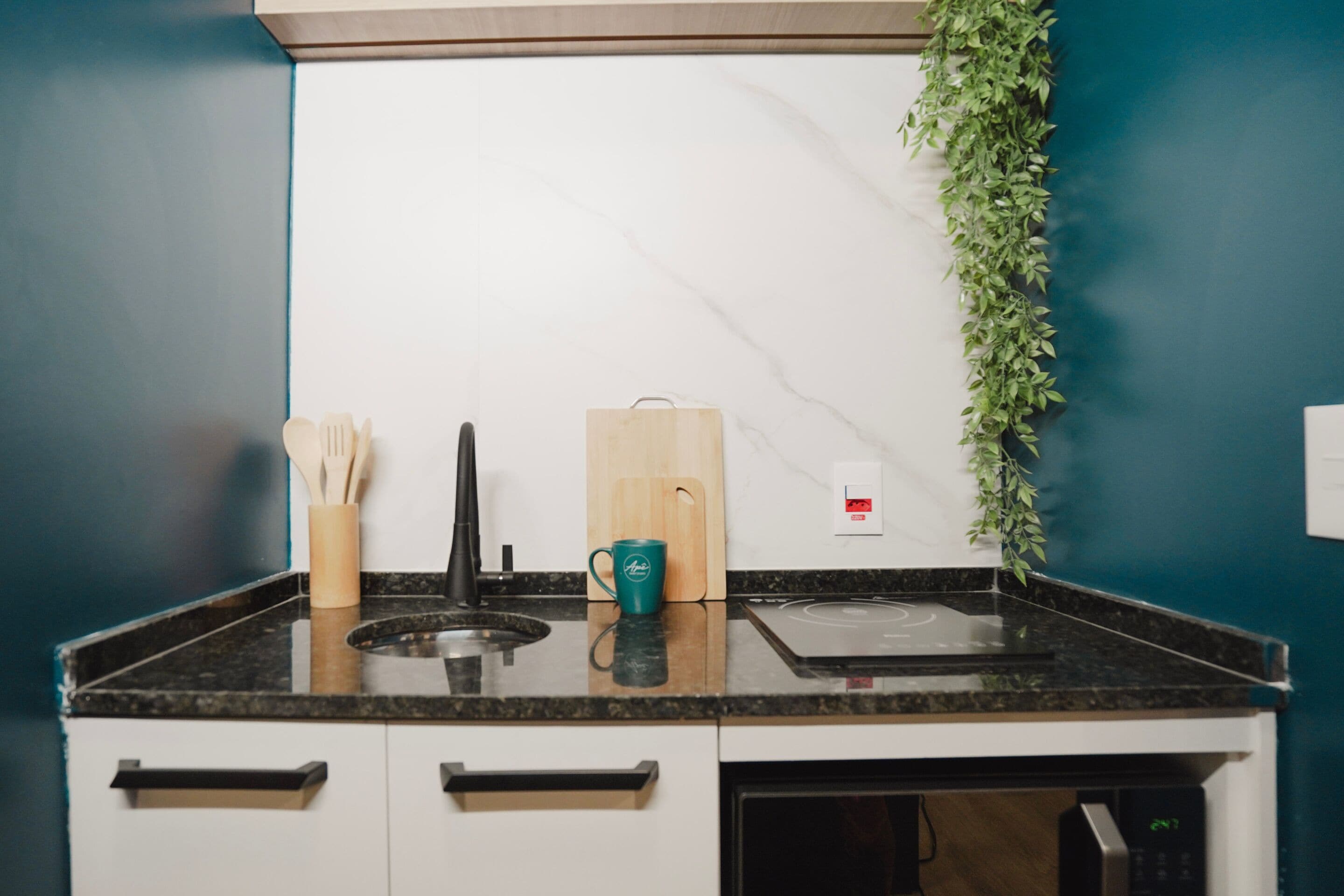 A kitchen with a black countertop, white cabinets, a microwave, and a wooden cutting board.
