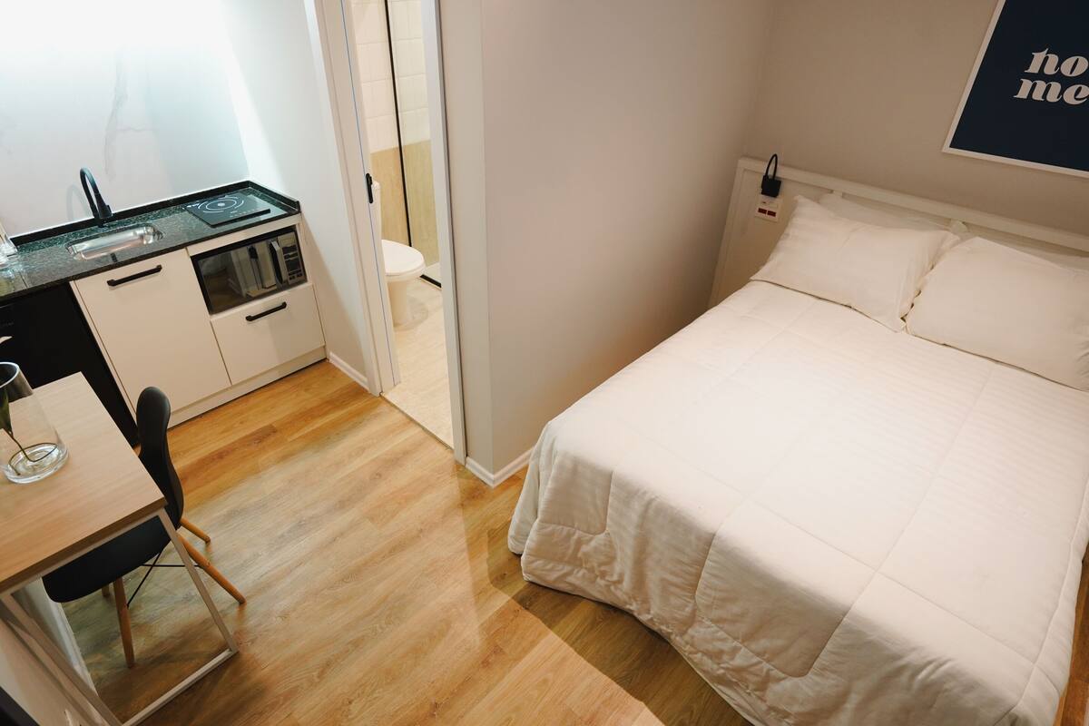 Ein kleines Schlafzimmer mit einem Bett, einer kleinen Küchenzeile und Holzboden.