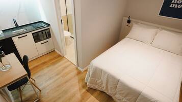 A compact bedroom with a bed, a small kitchenette, and a wooden floor.