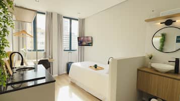 Una habitación de hotel moderna con cama, mesita de noche y una pequeña kitchenette.