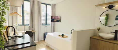 Una habitación de hotel moderna con cama, mesita de noche y una pequeña kitchenette.