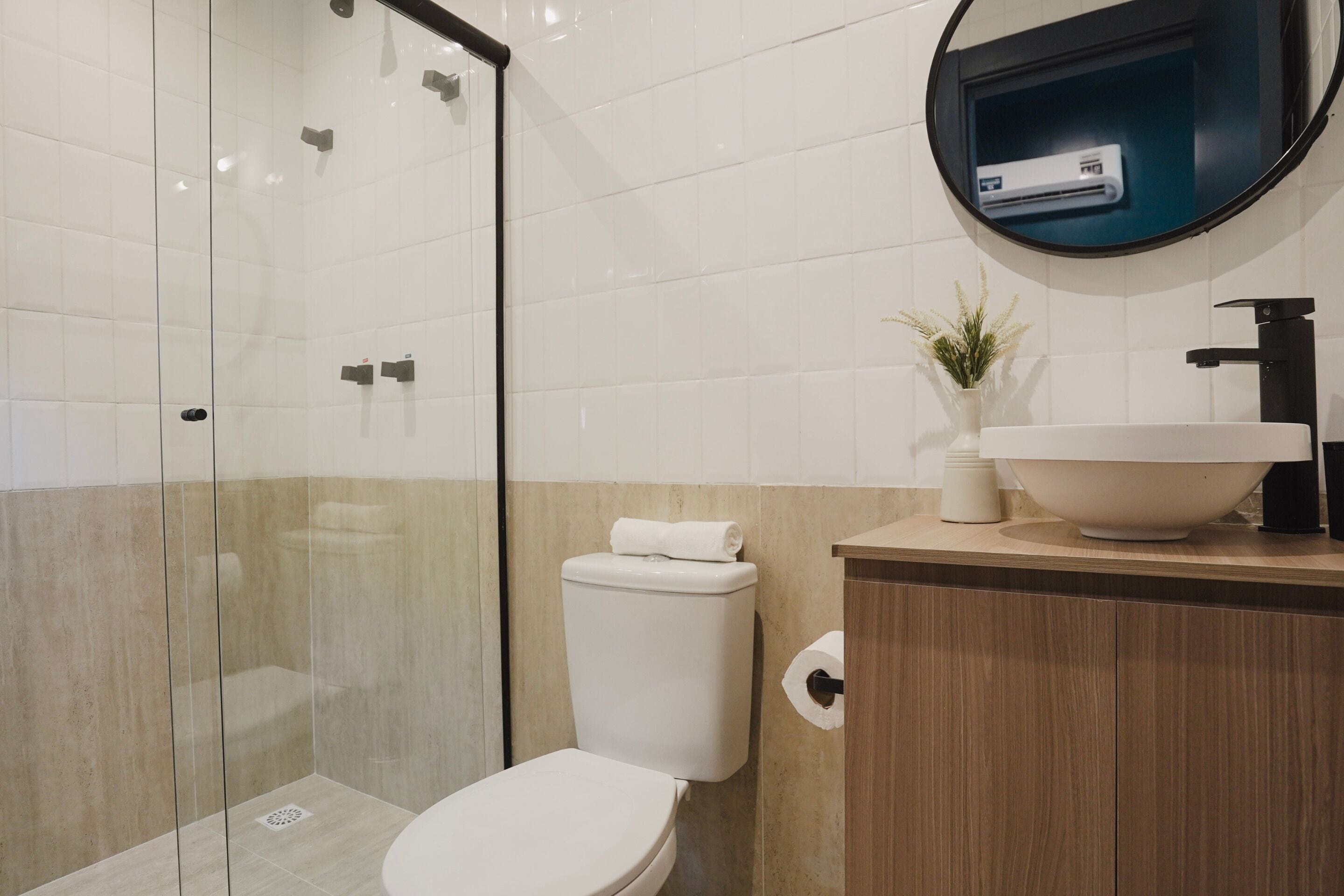 Un baño moderno con ducha envuelta en vidrio, inodoro blanco y tocador de madera con lavamanos y espejo.