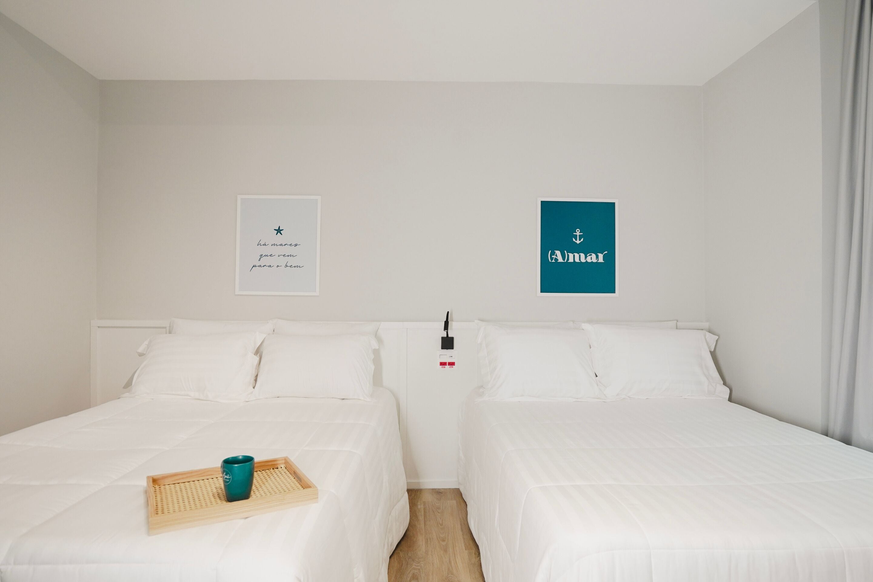 A hotel room with two beds, a wooden tray with a mug, and a wall-mounted sign.