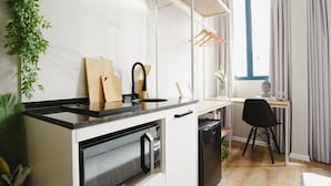 A modern kitchen with white cabinets, a black countertop, and a built-in oven. There is a wooden cutting board, a knife, and a black appliance. A black chair is visible in the background. - Apê Santos Gonzaga (Santos)