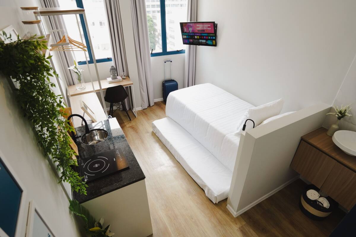 Ein kompaktes Hotelzimmer mit Bett, Küchenzeile, Fernseher und kleinem Badezimmer.