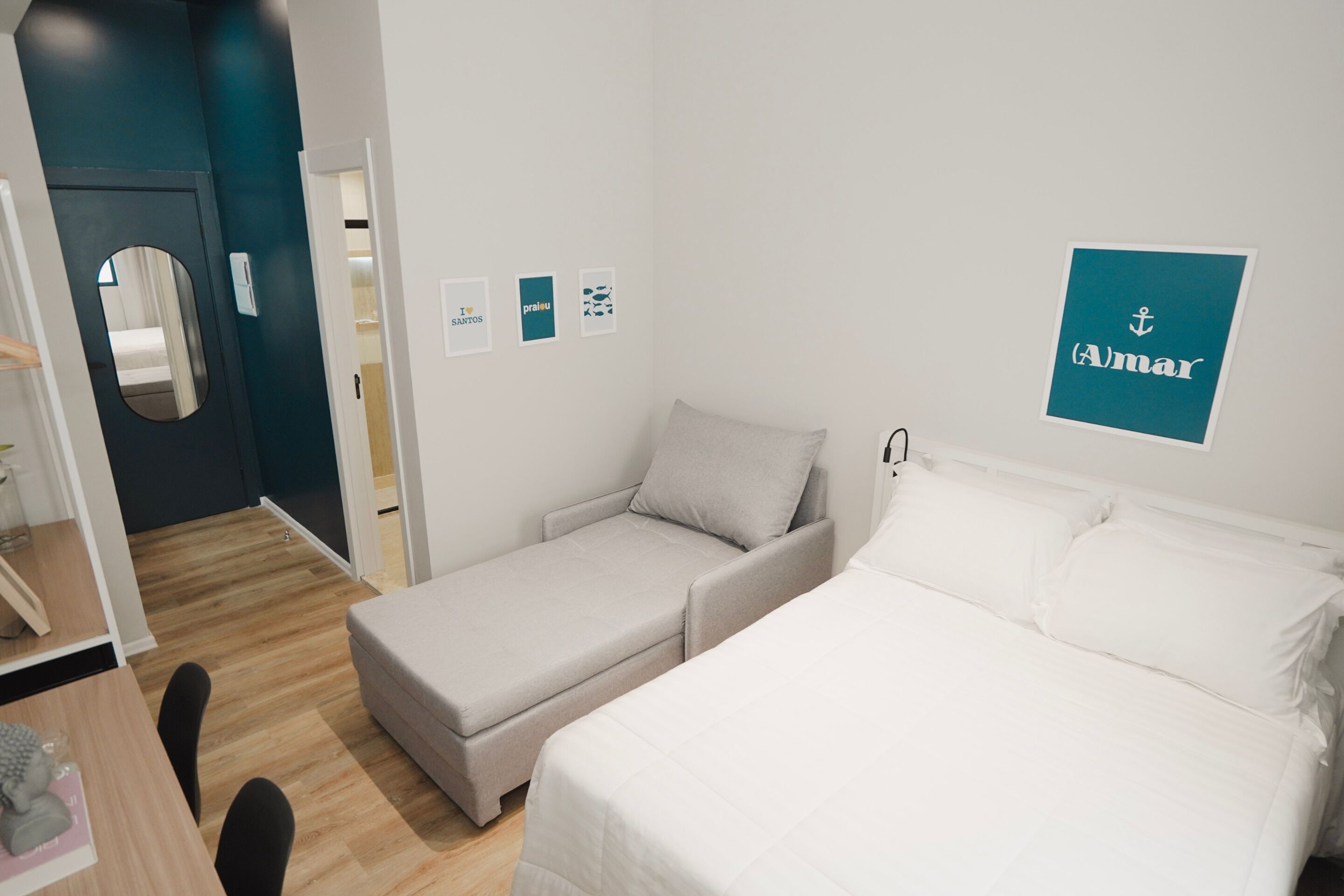 A hotel room with a bed, a sofa, a desk with a chair, and a mirror.