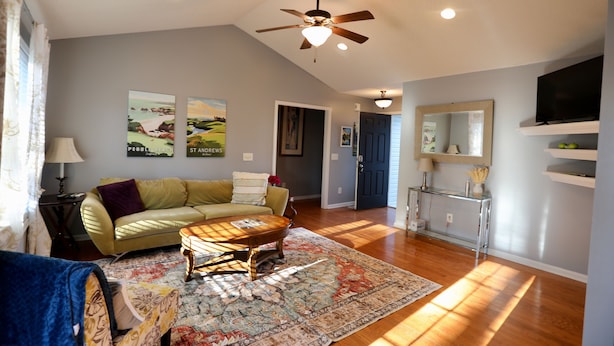 A living room with a sofa, coffee table, and a ceiling fan. There are framed pictures on the wall and a TV on a shelf. - 4-bedroom house in lovely Aberdeen so close to Pinehurst (Aberdeen)
