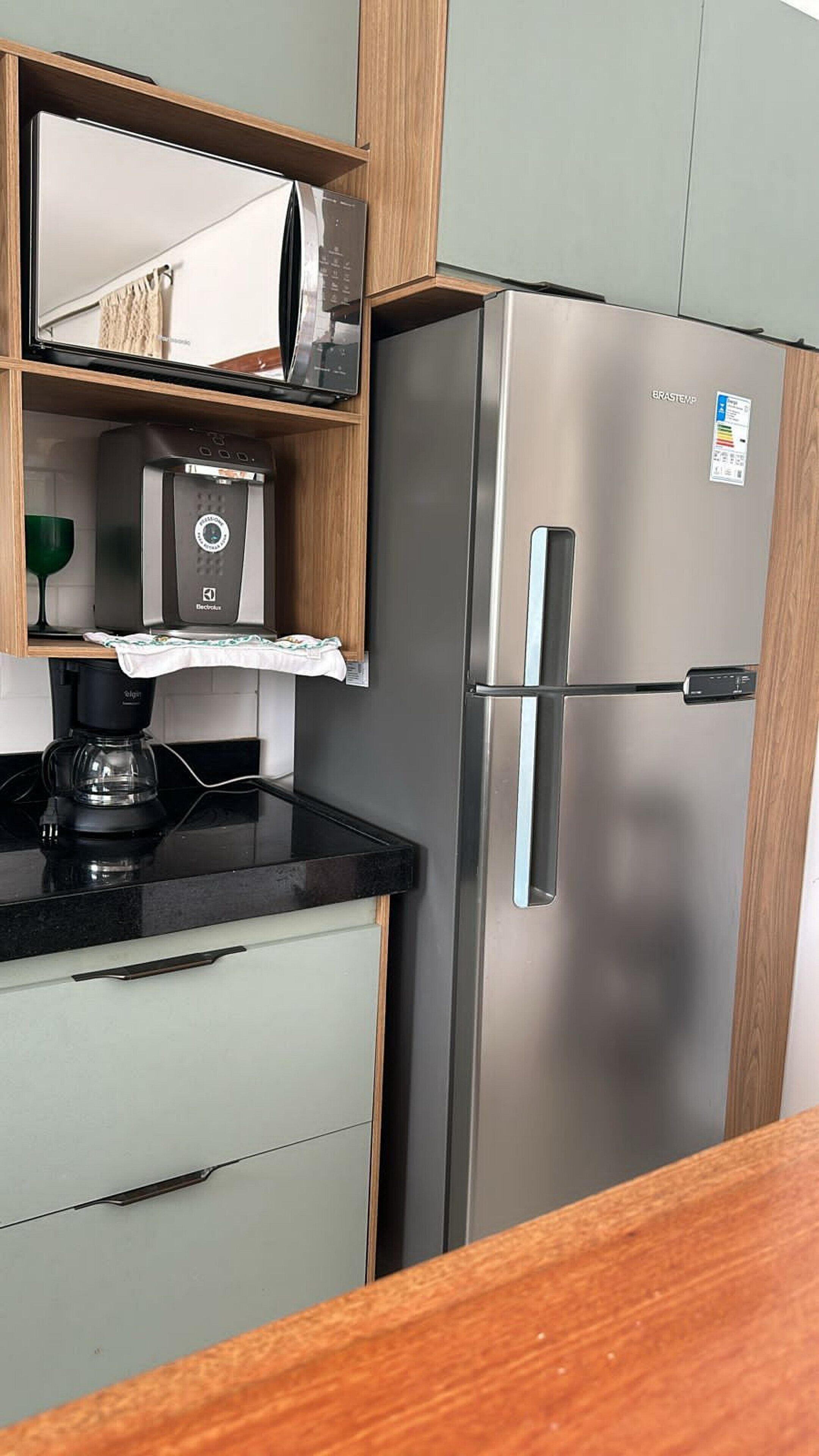 A kitchen with a stainless steel refrigerator, a coffee maker, and a microwave on a wooden shelf.
