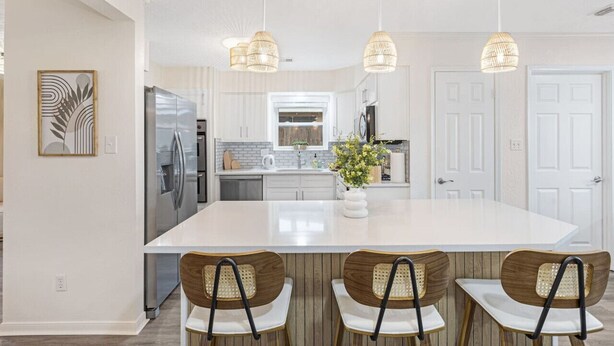 A modern kitchen with a large island, white cabinetry, and hanging pendant lights. - Relaxing Japandi Stay - Pool - Houston Stafford (Stafford)