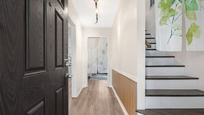 A hallway with a dark wooden door, a light wooden floor, and a staircase with a green leaf pattern on the wall. - Relaxing Japandi Stay - Pool - Houston Stafford (Stafford)