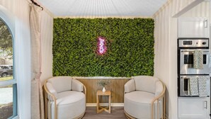 A room with two round chairs, a small wooden table, a neon sign, and a kitchen area with appliances. - Relaxing Japandi Stay - Pool - Houston Stafford (Stafford)