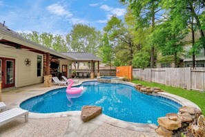 A backyard with a swimming pool, a pink flamingo float, and a covered patio area.