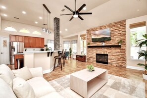 Amplia sala de estar con chimenea, cocina con armarios de madera y comedor con taburetes de bar.