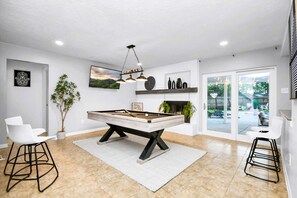 A pool table in a modern room with white walls, a large window, and a view of the outdoors.