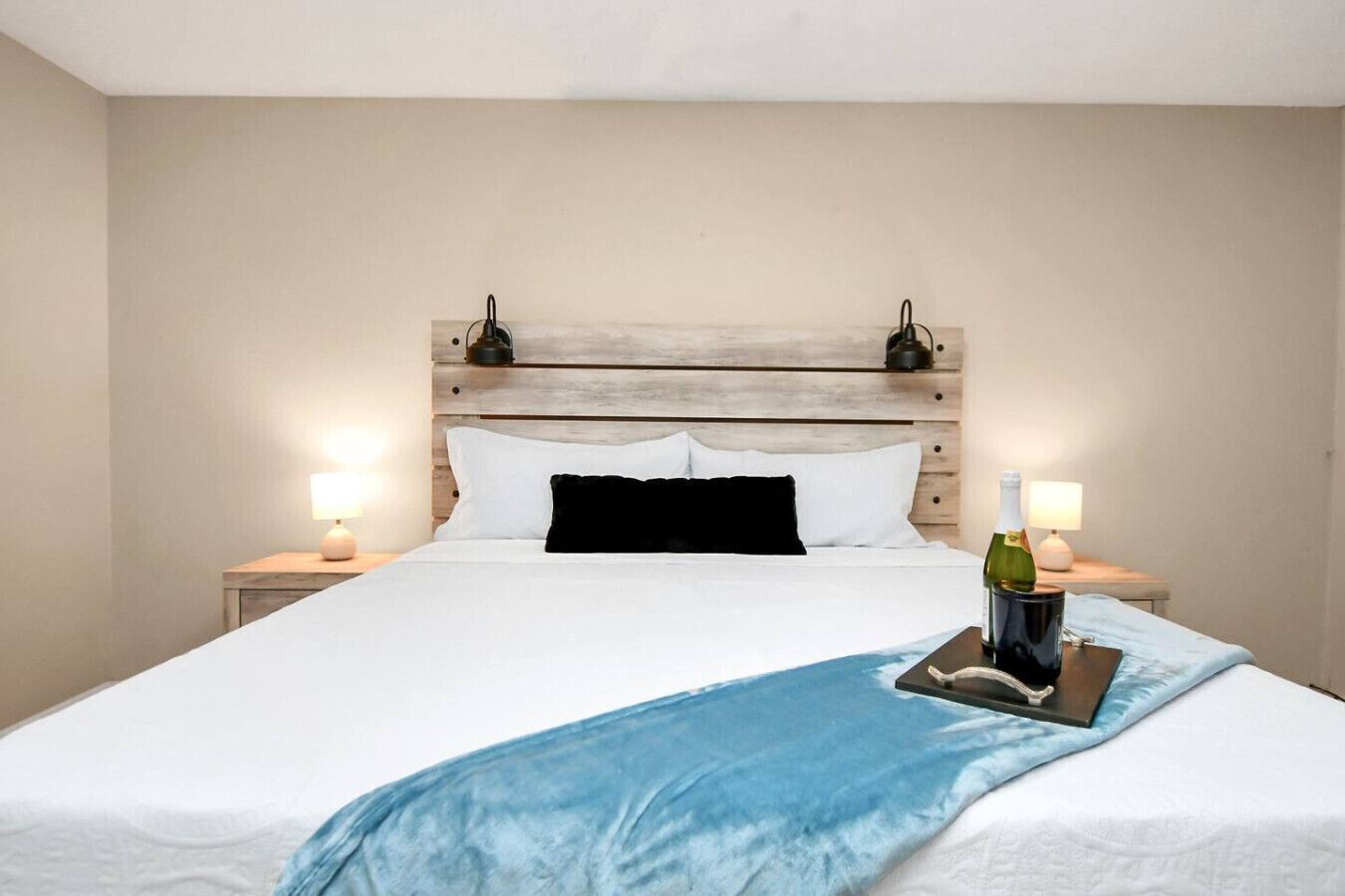 Ein Hotelzimmer mit einem großen Bett, einem Holzkopfstück, zwei Nachttischlampen und einer Weinflasche auf dem Bett.