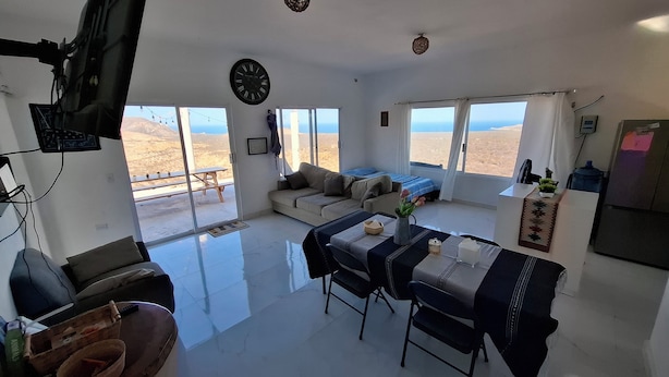 Un'ampia zona giorno con divani, un tavolo da pranzo con sedie, una televisione a parete e ampie finestre che offrono vista sul paesaggio desertico.