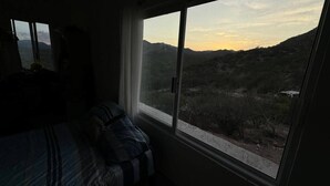 Camera da letto con una grande finestra che si affaccia su un paesaggio montuoso al tramonto.