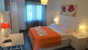 Une chambre d’hôtel comprenant un lit, deux tables de chevet, un bureau avec une chaise, une télévision et une fenêtre avec des rideaux.