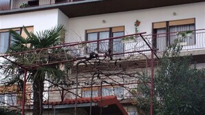 Un immeuble à plusieurs étages, doté d’une façade en pierre, de balcons et d’un petit jardin agrémenté de plantes et de fleurs.