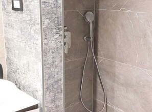 Een douche met een handdouche en een bedieningspaneel aan de muur.