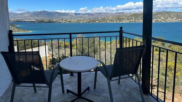 A balcony with a table and chairs, overlooking a body of water and distant mountains. - House by the sea (Salamina)