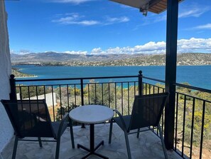 Un balcon avec une table et des chaises, donnant sur une étendue d’eau et sur des montagnes lointaines.