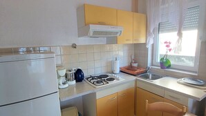 A compact kitchen with a refrigerator, stove, and sink. There is a window with a view of the outdoors. - Elegant Apartments with Sea View and Balcony - One Bedroom Apartment with Sea View and Balcony (Crikvenica)