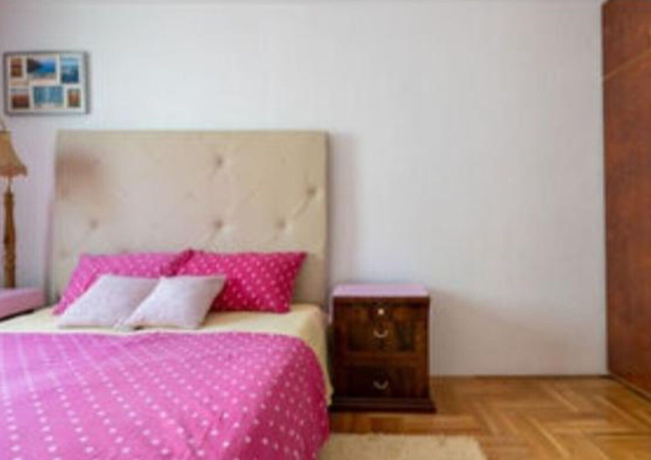 A bedroom with a bed, a nightstand, and a wooden floor.