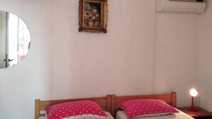 A bedroom with two beds, a round mirror, a wall-mounted air conditioner, and a framed picture.