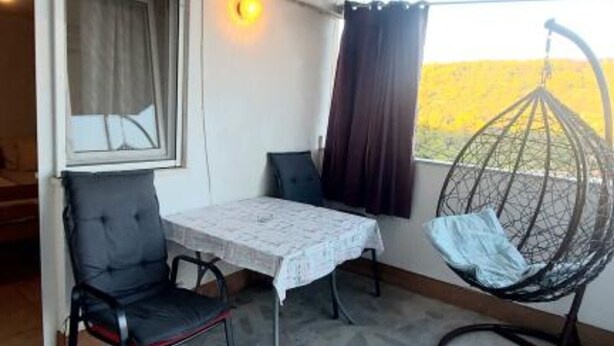 A small balcony with a table, chairs, a hanging chair, and a view of the outdoors.