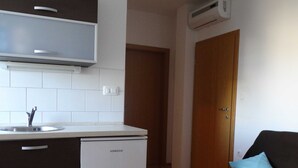 A compact kitchen with white cabinets, a Koncar refrigerator, a built-in sink, and a wooden door leading to another room.