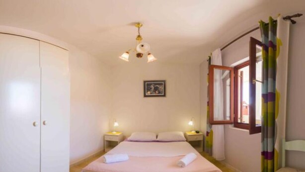 A bedroom with a single bed, bedside tables, a wardrobe, a window with curtains, and a ceiling light fixture. - Apartments Jukica - Three Bedroom Apartment With Sea View (Vis)