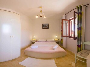 A bedroom with a single bed, bedside tables, a wardrobe, a window with curtains, and a ceiling light fixture.