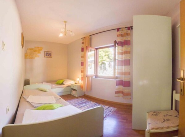 A room with two beds, a window with curtains, a desk, and a chair.