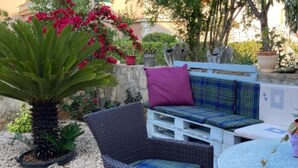 A wicker chair with a cushion, a small round table, and a potted plant with red flowers. - Apartments Jukica - Three Bedroom Apartment With Sea View (Vis)