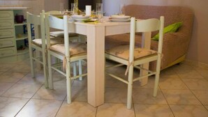 A dining area with a white table and chairs, a sofa with a green pillow, and a television in the background. - Apartments Jukica - Three Bedroom Apartment With Sea View (Vis)