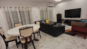 A modern living room with a dining area, a sofa, a TV, and a fireplace. - 3-ROOM APARTMENT WITH BALCONY TERRACE GARDEN SWIMMING POOL (Abidjan)