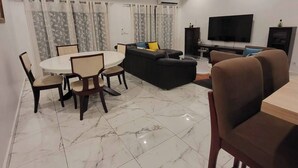 A modern living room with a dining area, a sofa, a TV, and a fireplace. - 3-ROOM APARTMENT WITH BALCONY TERRACE GARDEN SWIMMING POOL (Abidjan)