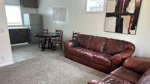 A living room with a brown leather sofa, a dining table with chairs, a kitchen area with cabinets and a refrigerator, and a painting on the wall. - Family and Dog Friendly Modern Traditional Home in Rapid City South Dakota (Rapid City)