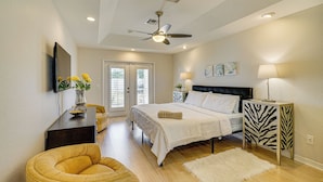 A bedroom with a bed, a ceiling fan, a bedside table with a lamp, a chair, and a door leading to another room. - 4 Mi to Beach: Home w/ Patio in Cape Coral! (Cape Coral)