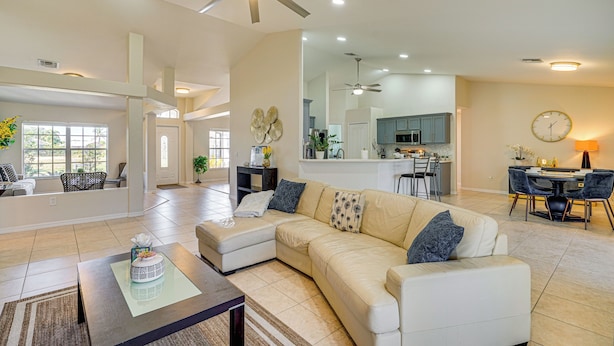A spacious living area with a large beige sectional sofa, a coffee table, and a ceiling fan. - 4 Mi to Beach: Home w/ Patio in Cape Coral! (Cape Coral)