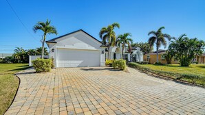 A residential house with a garage, paved driveway, and palm trees. - 4 Mi to Beach: Home w/ Patio in Cape Coral! (Cape Coral)