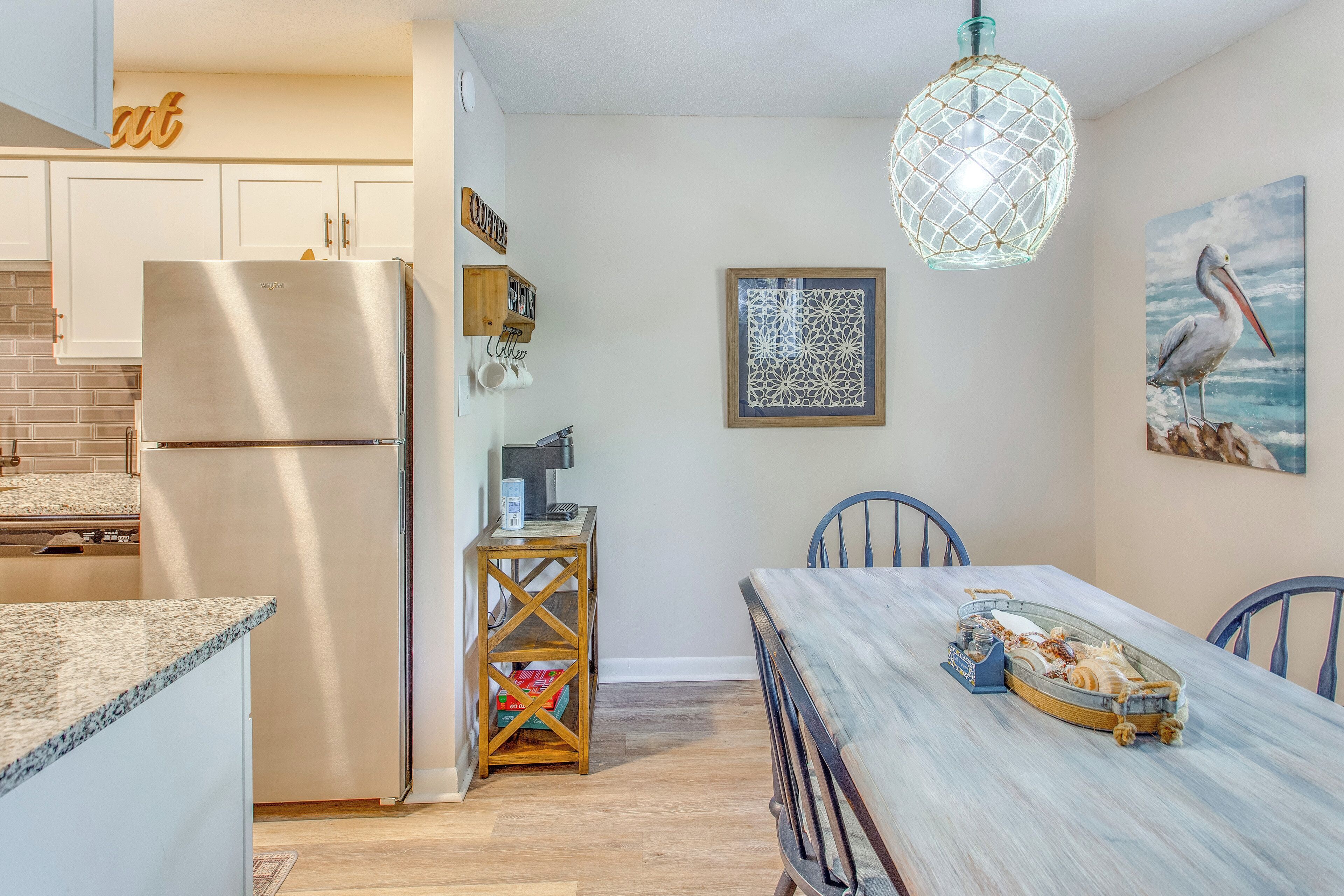 A kitchen with a stainless steel refrigerator, wooden cabinets, a dining table with chairs, and a hanging light fixture.