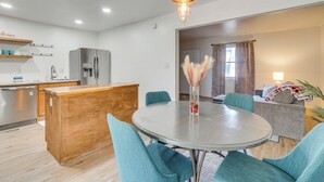 Une cuisine moderne avec un îlot central, un coin repas avec des chaises de couleur turquoise et un salon avec un canapé et une lampe.