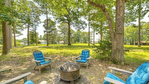 Un terrain de camping équipé de quatre chaises Adirondack, d’un foyer en métal et entouré d’arbres.