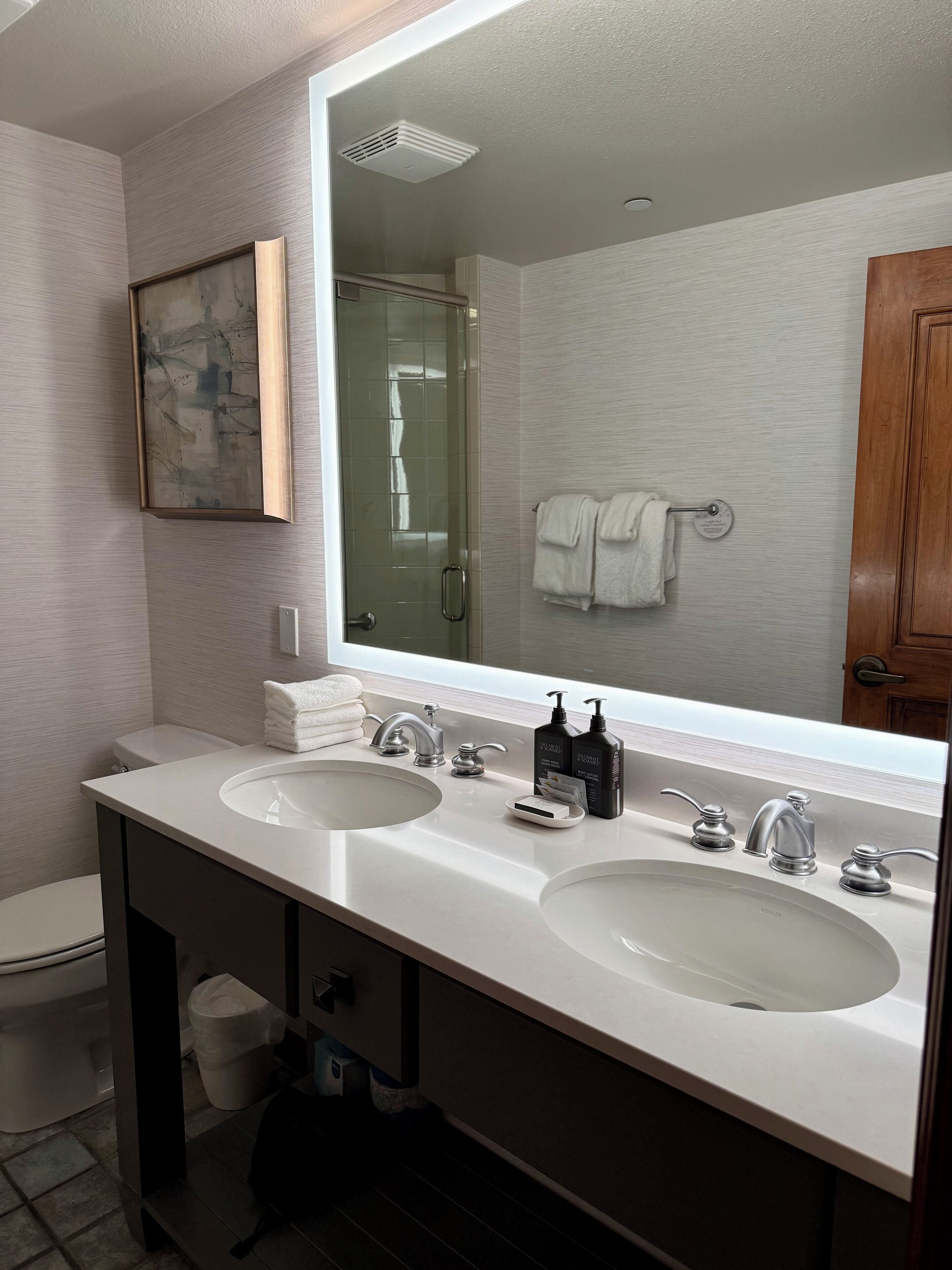 A modern bathroom with two sinks, a large mirror, and a shower visible in the reflection.