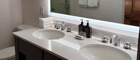 A modern bathroom with two sinks, a large mirror, and a shower visible in the reflection.
