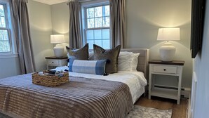 A neatly made bed with a striped blanket, two bedside tables with lamps, and a wicker basket on the bed. - 12 Mins from Beach - A Quiet, Immaculate space (Norwell)